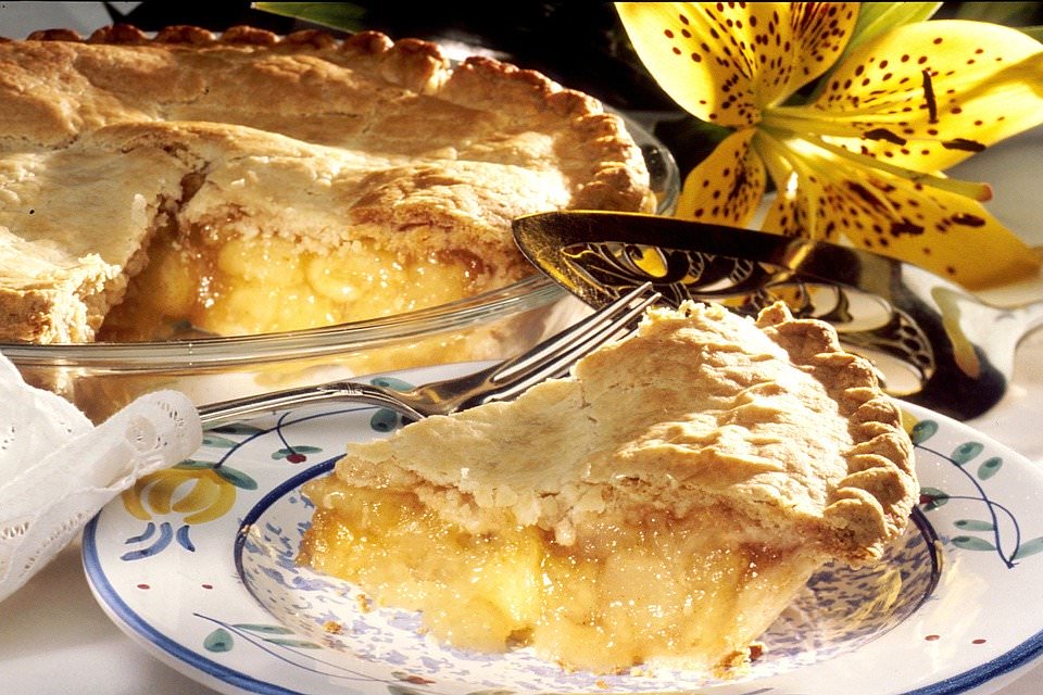 A plated slide of apple pie with the whole pie in the background.