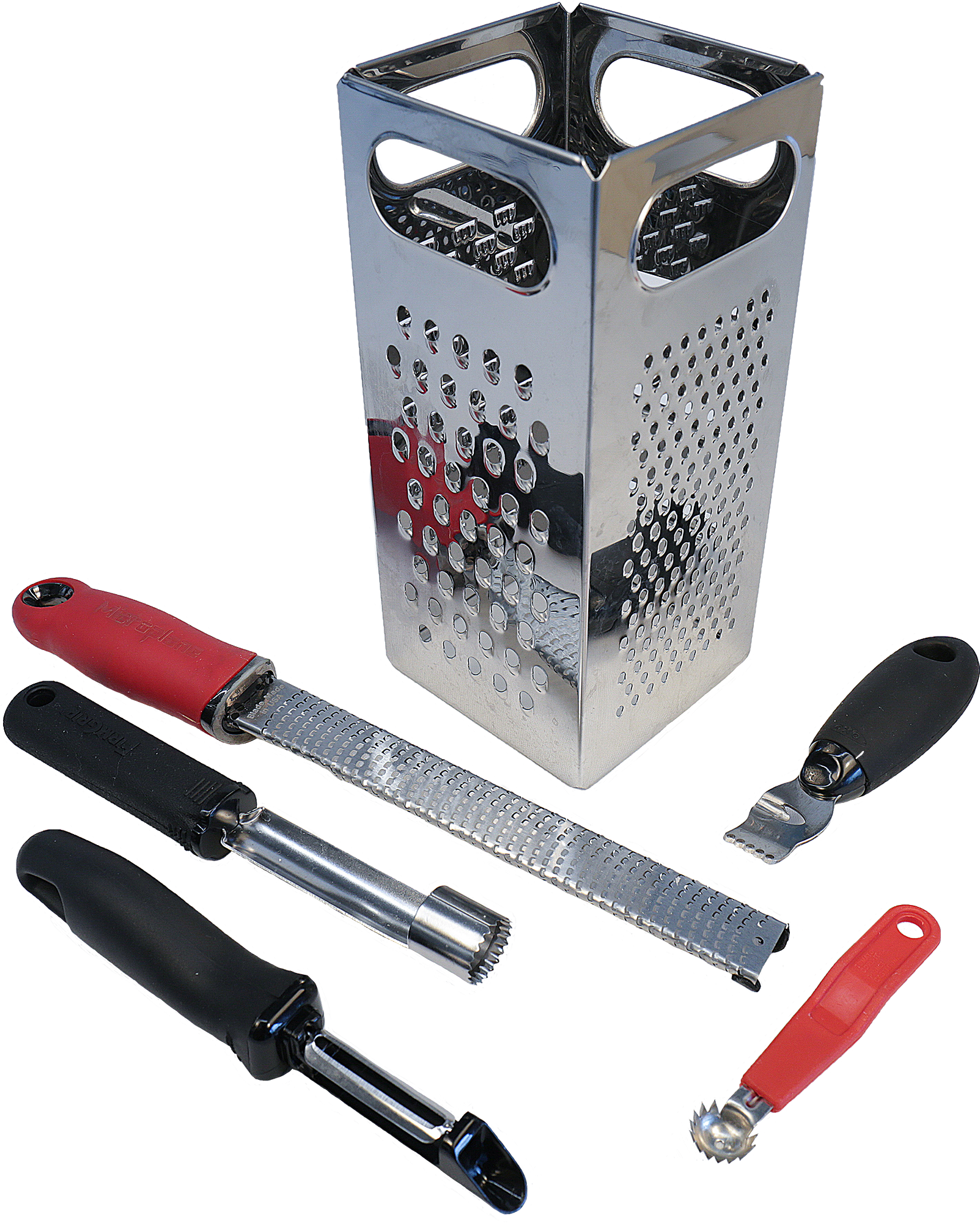 6 types of shredding and peeling devices. Stainless steel box grater in the background with 4 sides that have different course shredding edges. On the right, a black handled zester with a black oval handle and stainless-steel head, flat, with 5 small holes. Underneath, a tomato shark with a red handle, made of plastic, a rounded serrated head. On the left, in the foreground, a black, straight vegetable peeler, followed by an apple corer with a black handle and long stainless-steel shaft. In the background, a microplane with a red handle, long flat shaft, with fine raised blades.