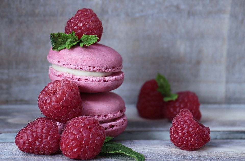 An arrangement of fresh raspberries, mint leaves, and cream filled macarons. 