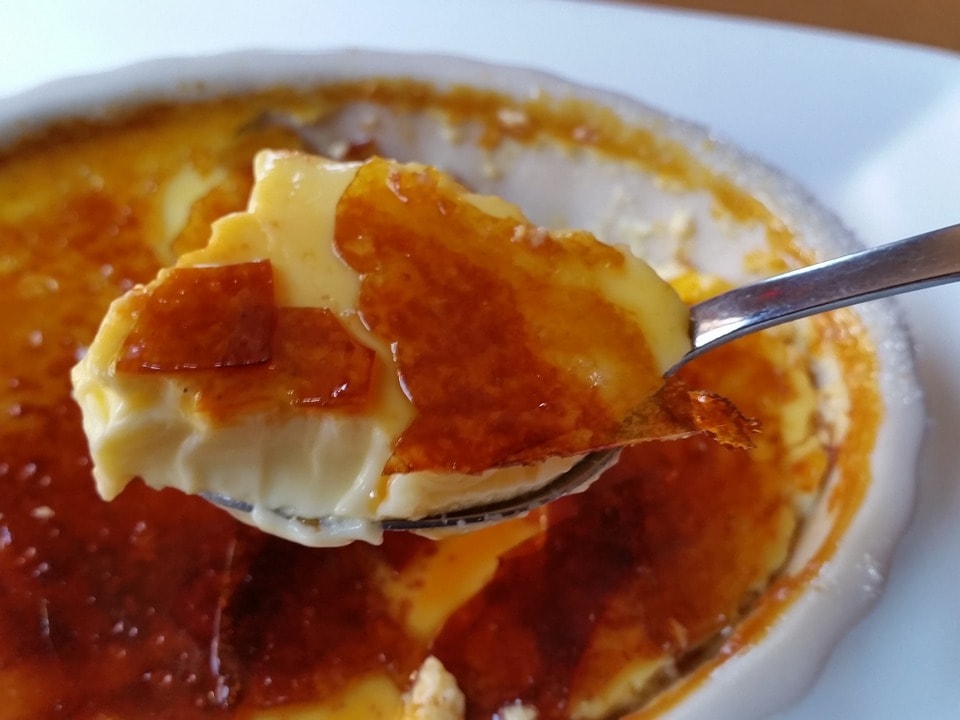 A spoon full of crème brulee over top of a partially eaten crème brulee.