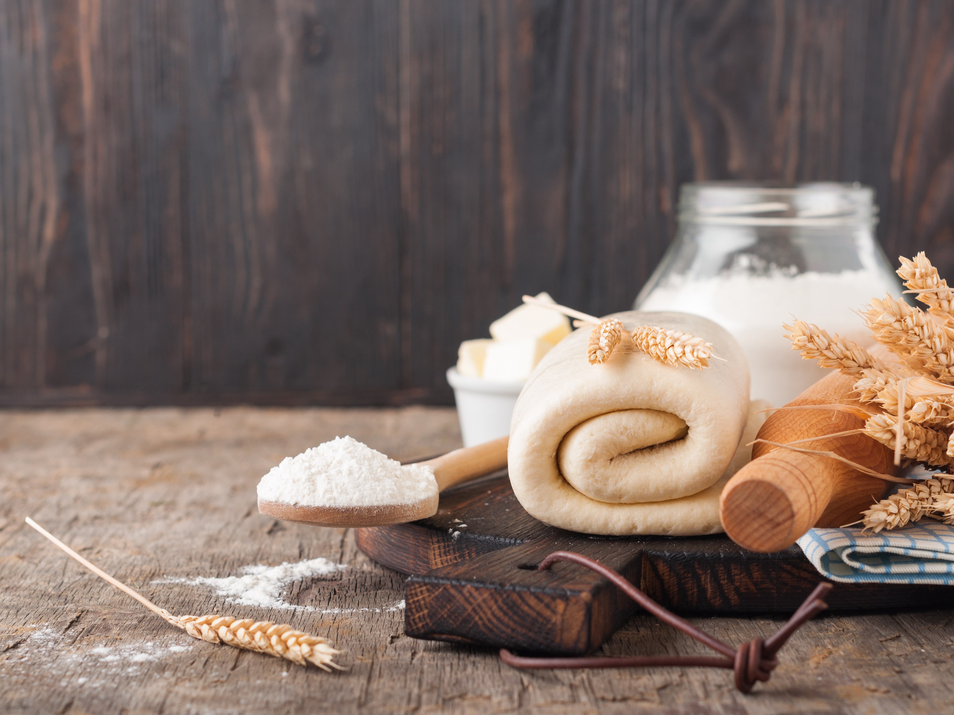 Folded raw puff pastry on a wooden cutting board on a rustic wooden table. Dough's rolls with a rolling pin, flour, butter, wheat spikelets.