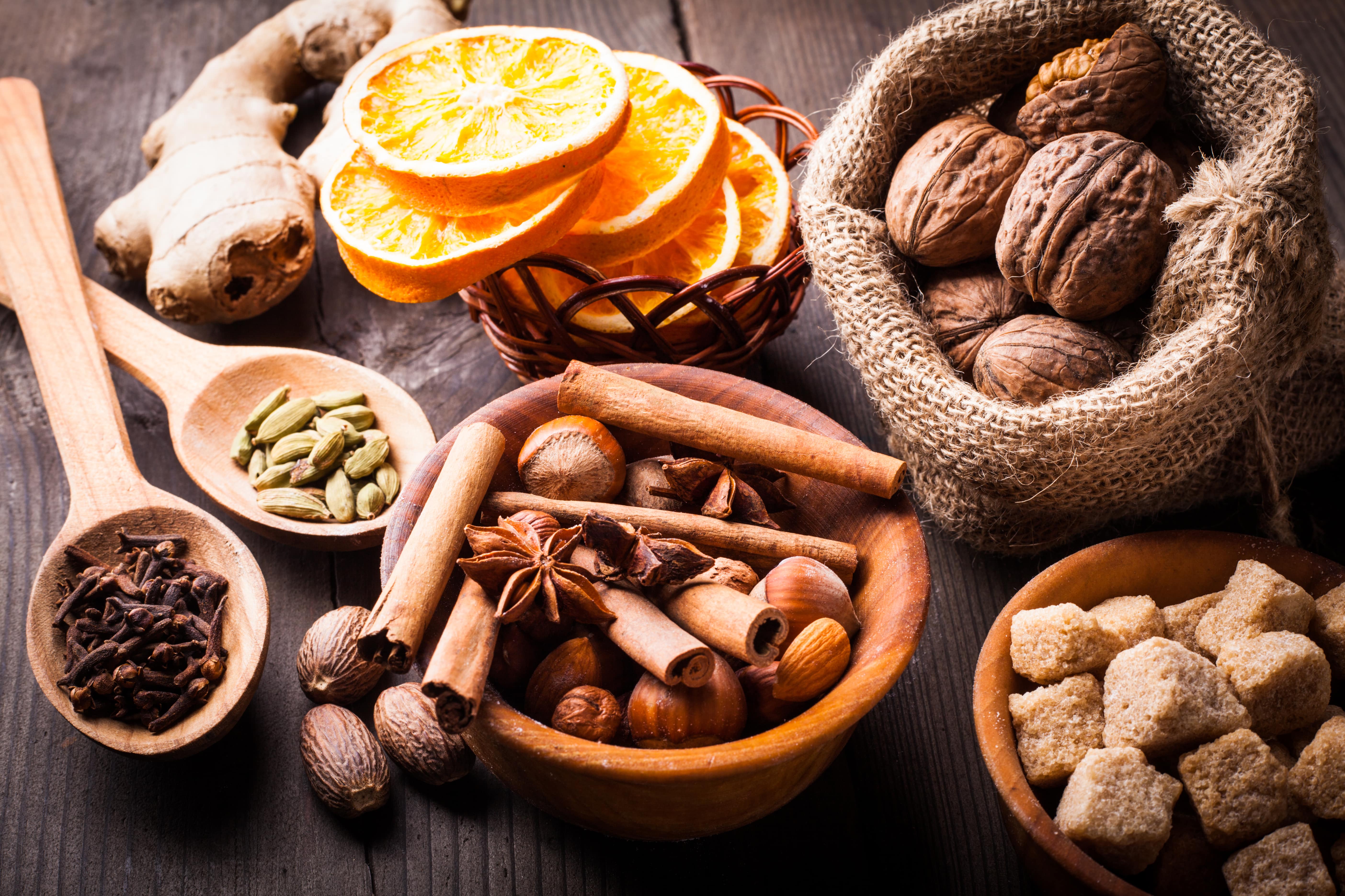 nuts, brown sugar, dried orange, kandamon, cloves, cinnamon, nutmeg, ginger and anise on a wooden table.