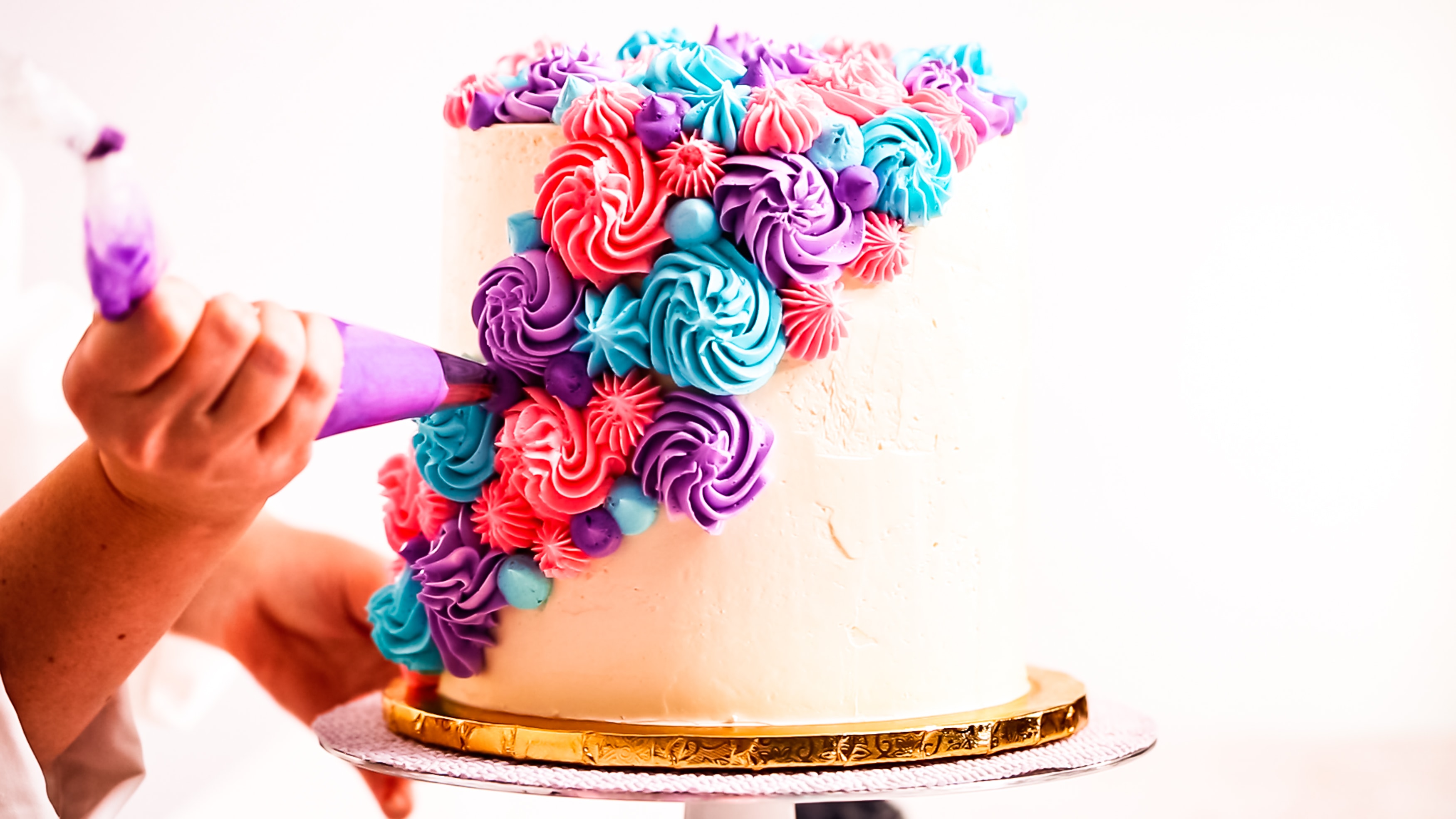 Baker piping pastel color buttercream rosettes on a white cake.