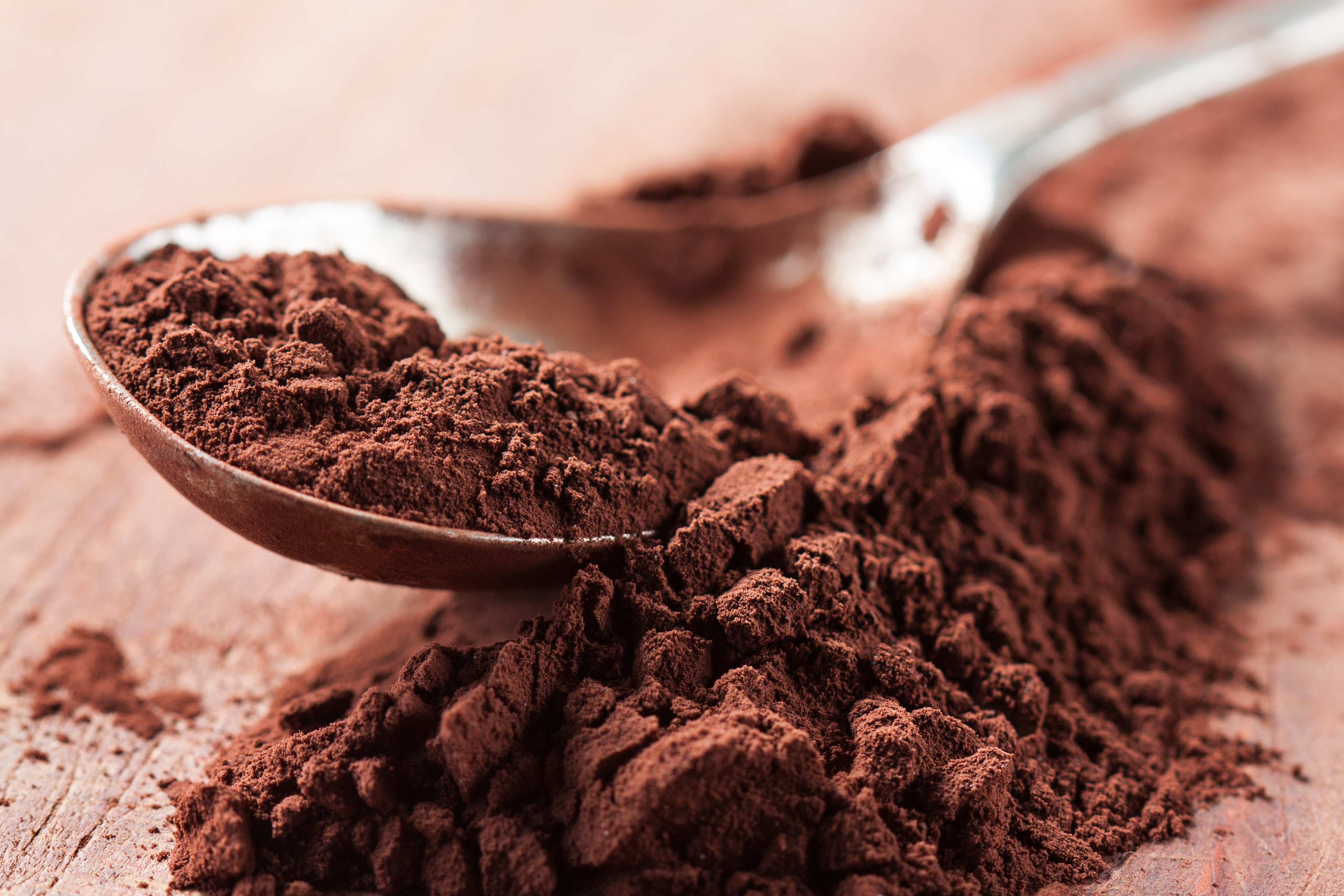 Cocoa powder on a spoon over a wooden table.