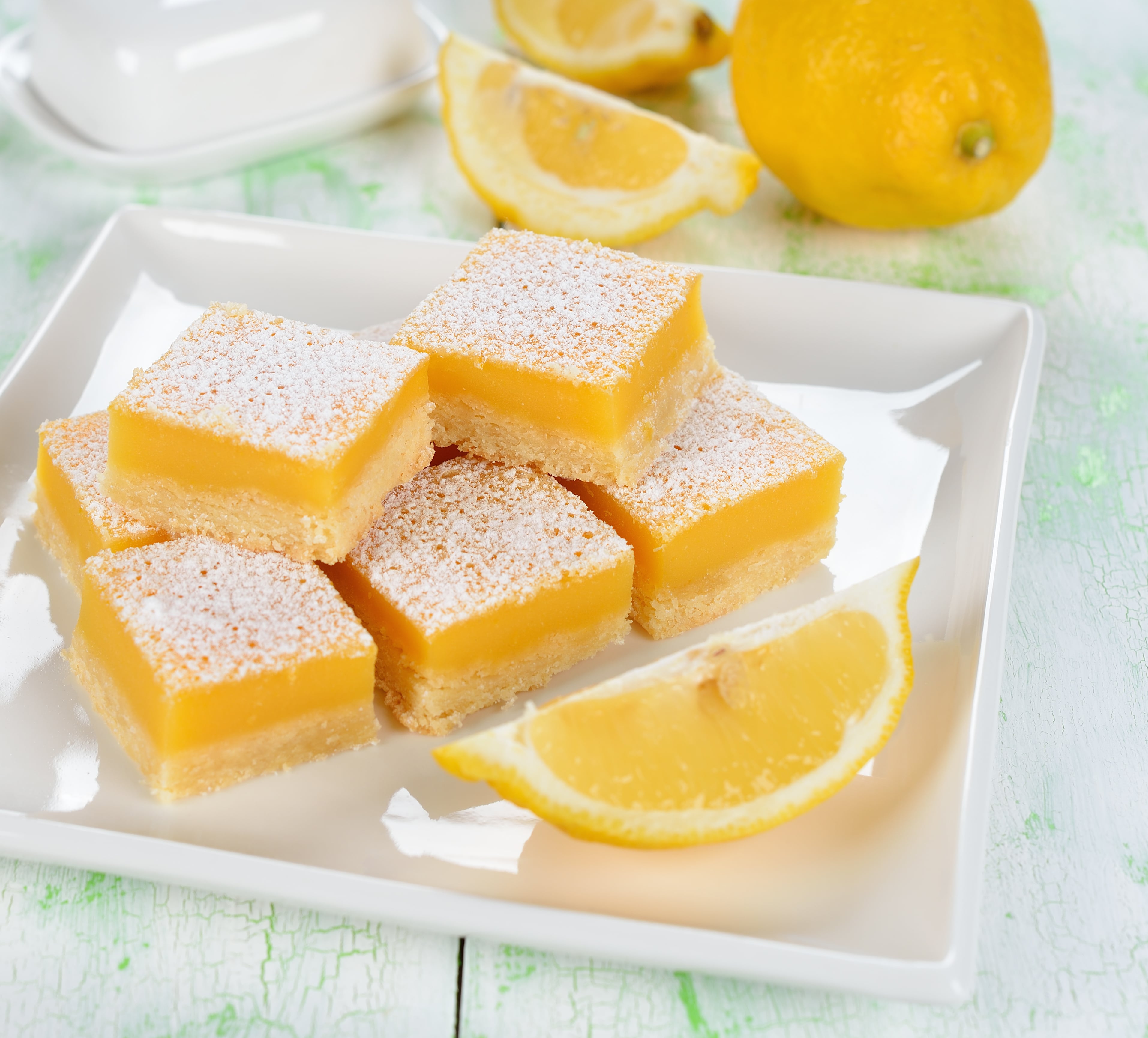Traditional lemon bars with a slice of lemon on a white plate.