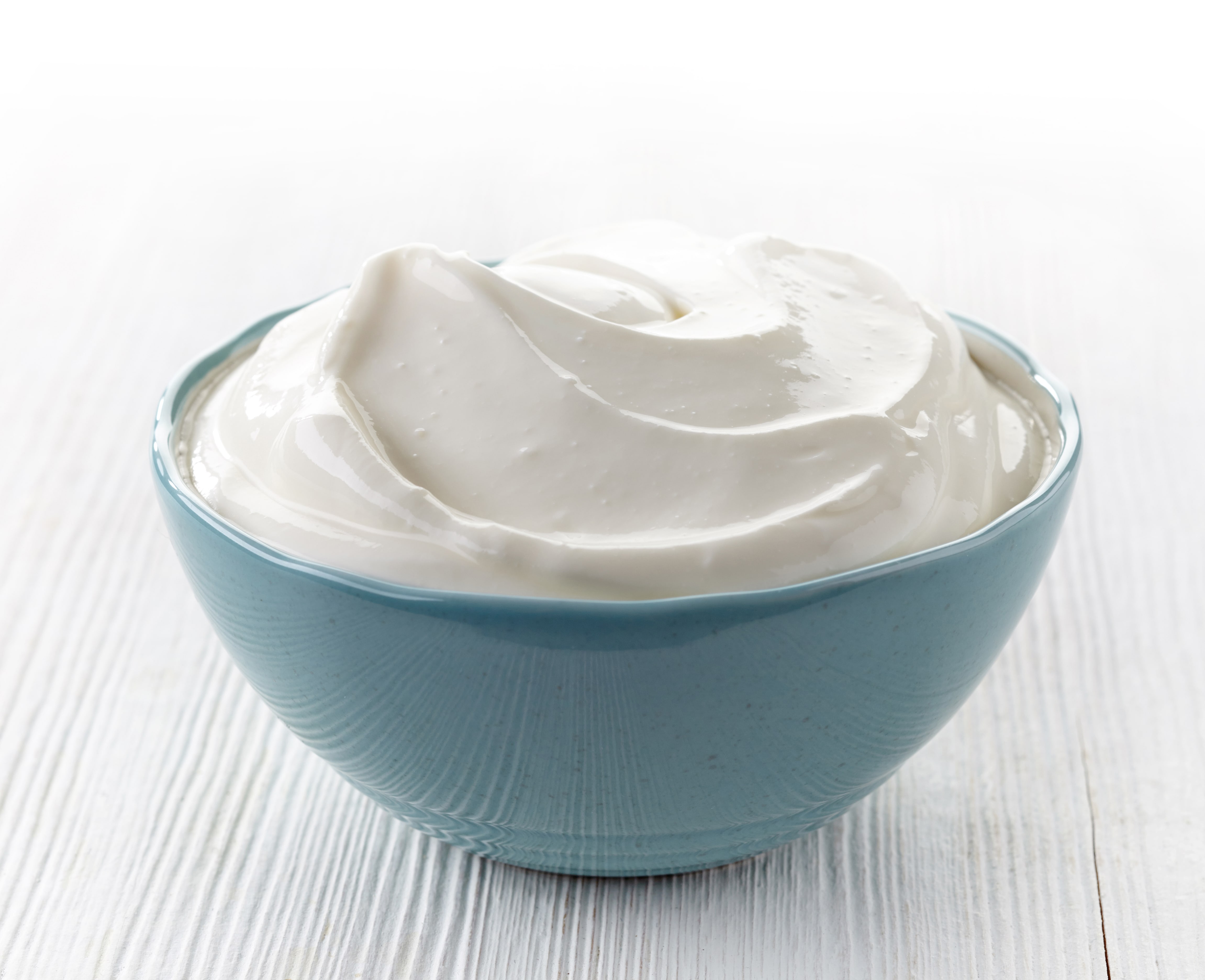Bowl of sour cream on white wooden table.