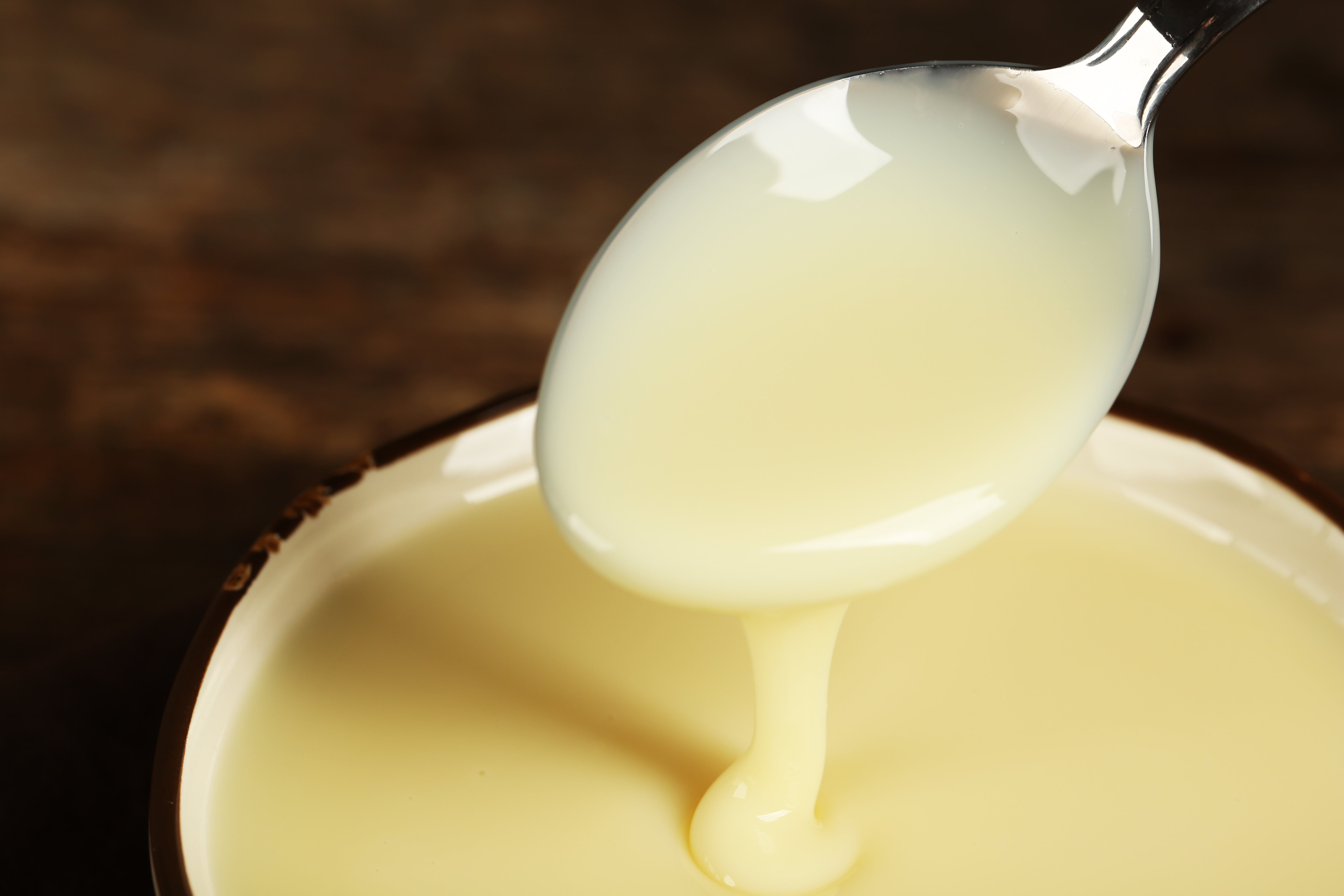 Bowl with condensed milk and spoon on table.
