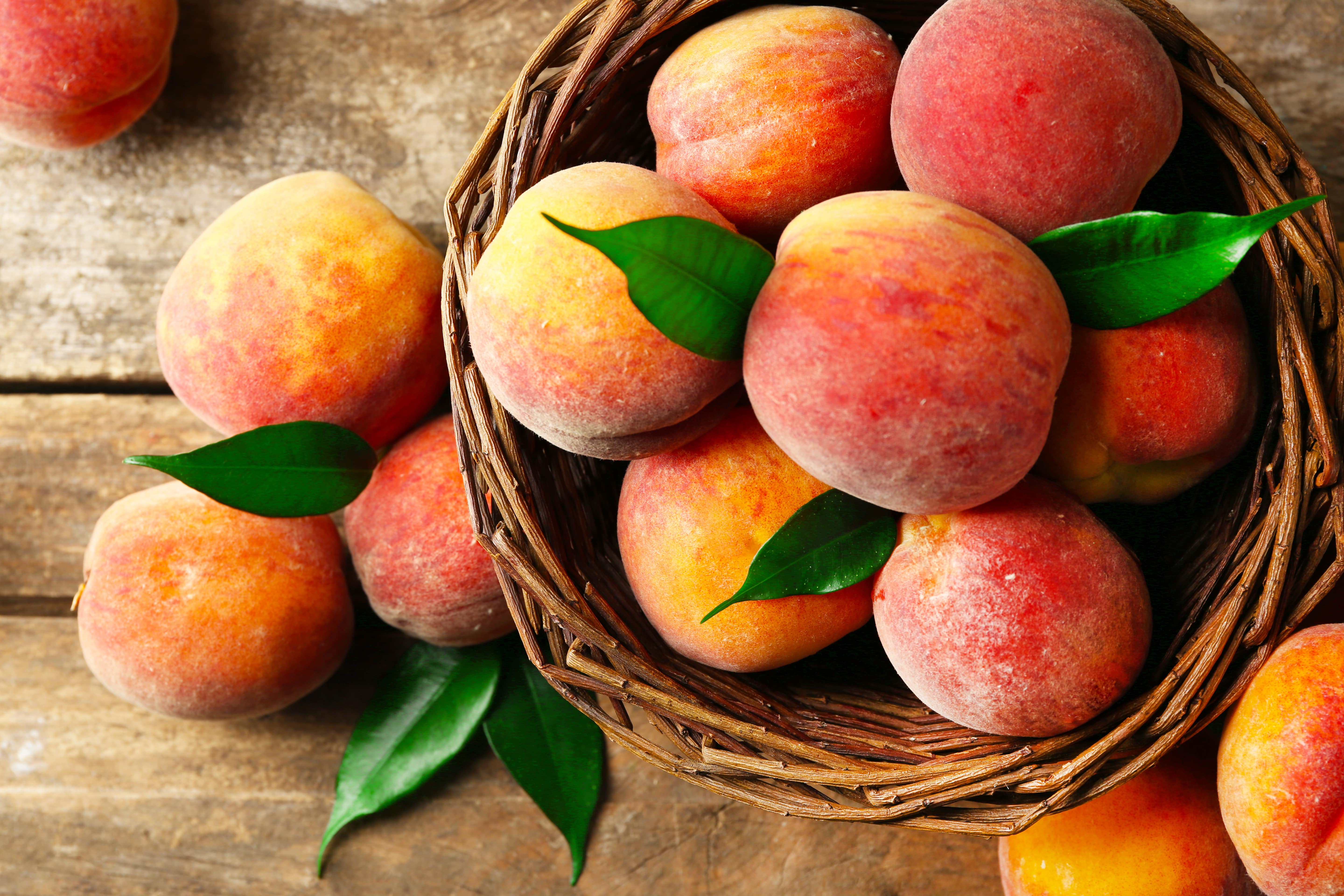 Ripe peaches in basket on wooden background.