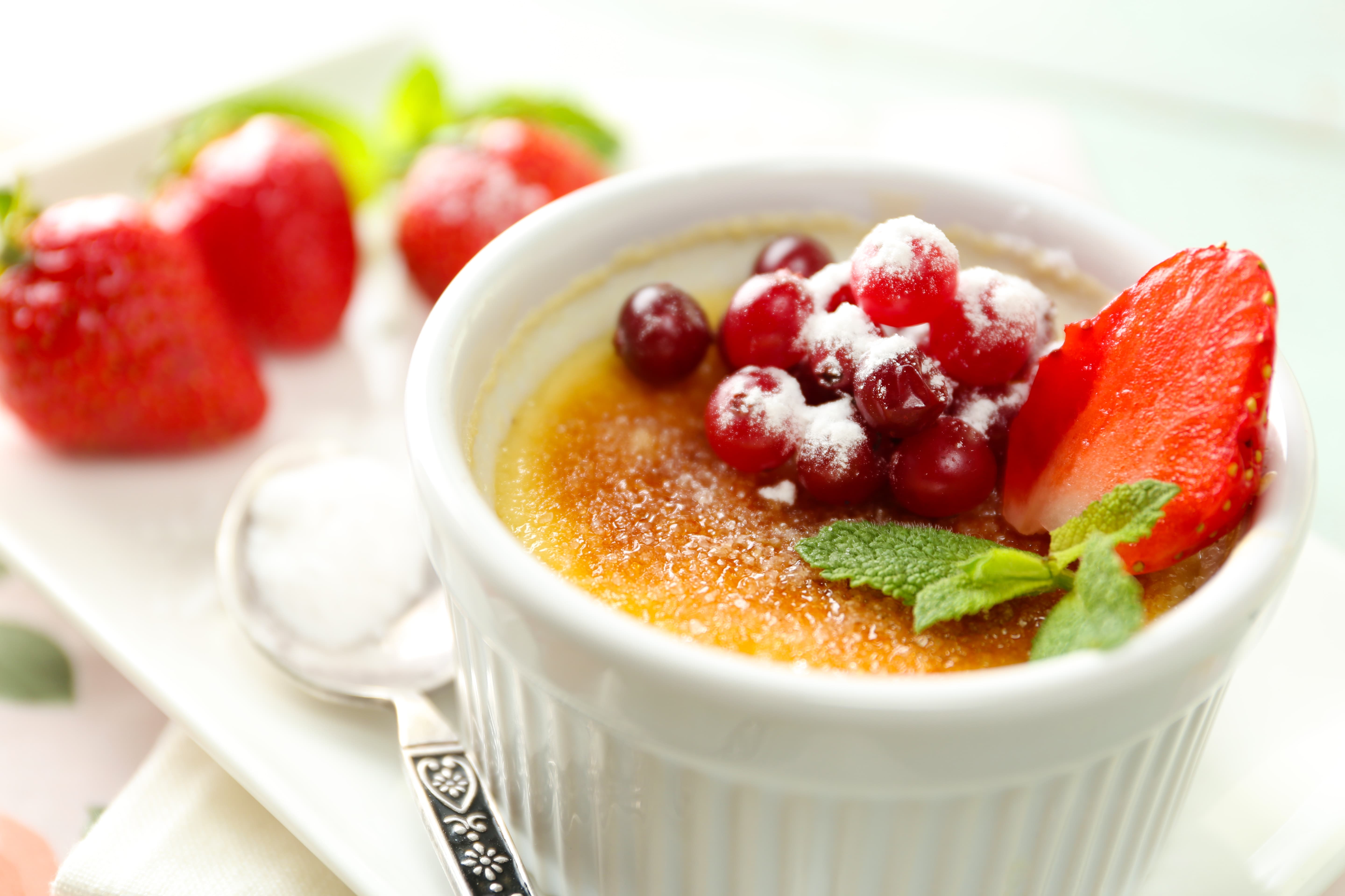 Creme brulee dessert with fresh strawberries and mint leaves, on color wooden background.