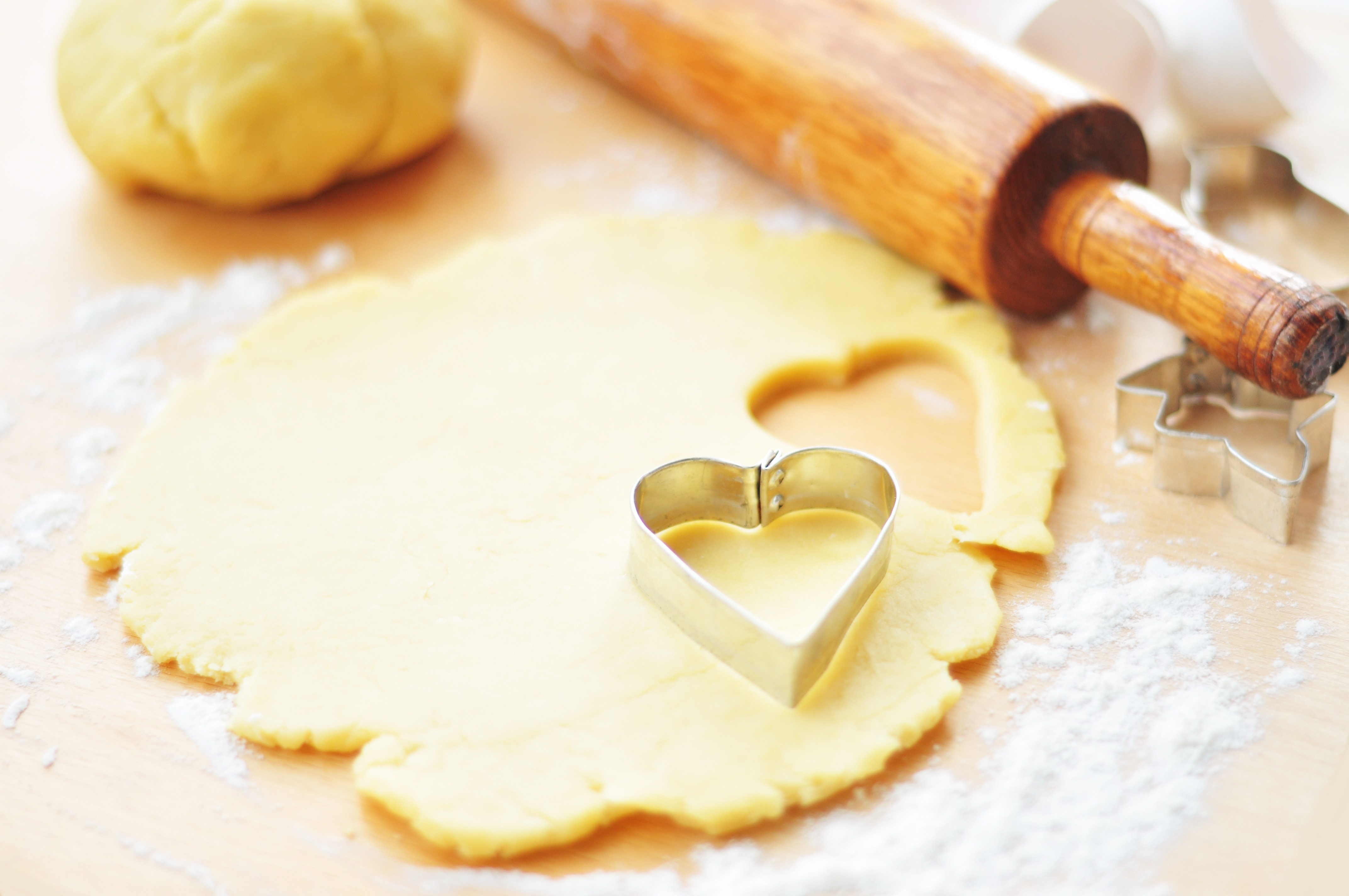 Rolled out cookie dough with a rolling pin and a cookie cutter on a wooden surface.