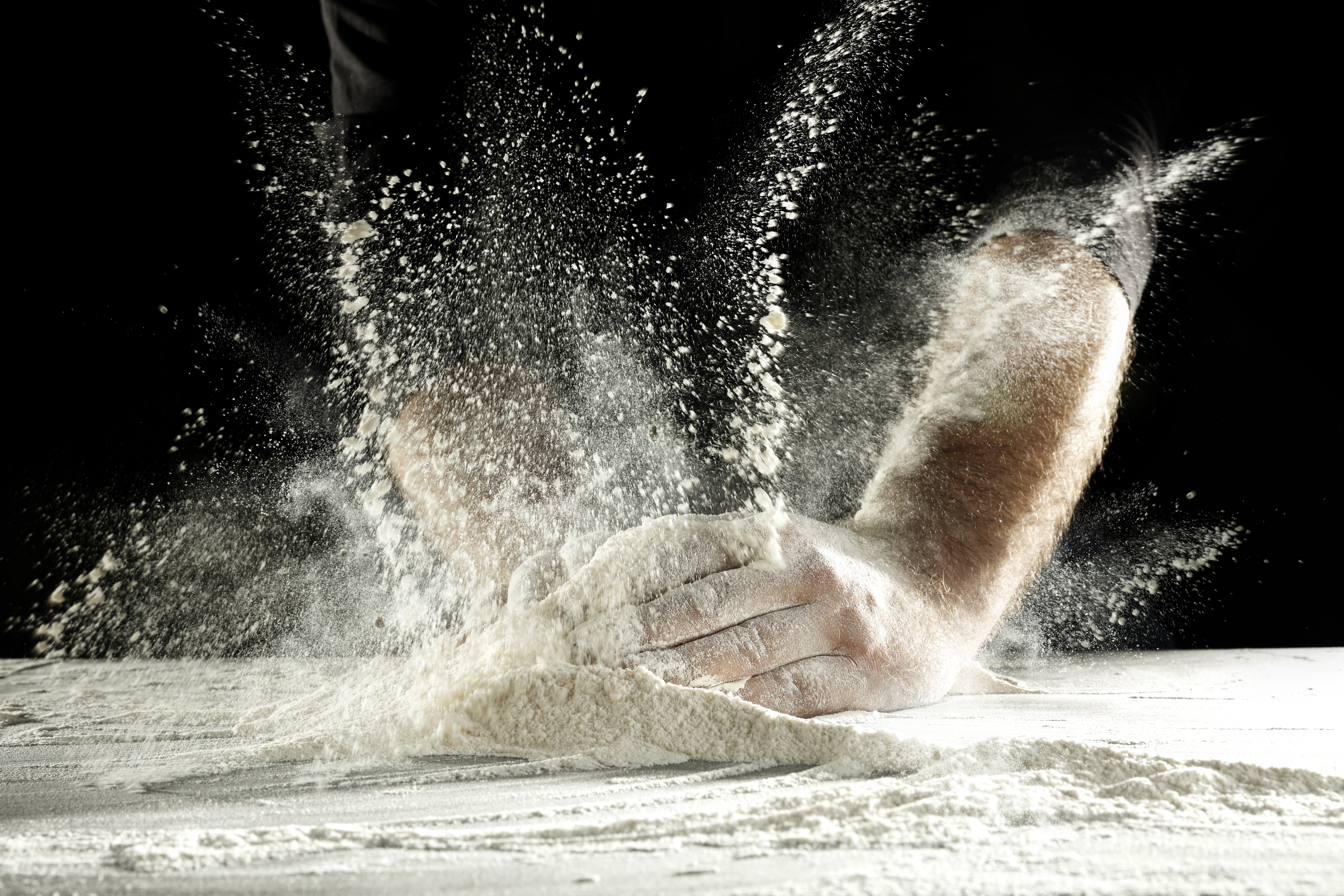 Hands with splash of white flour and black background.