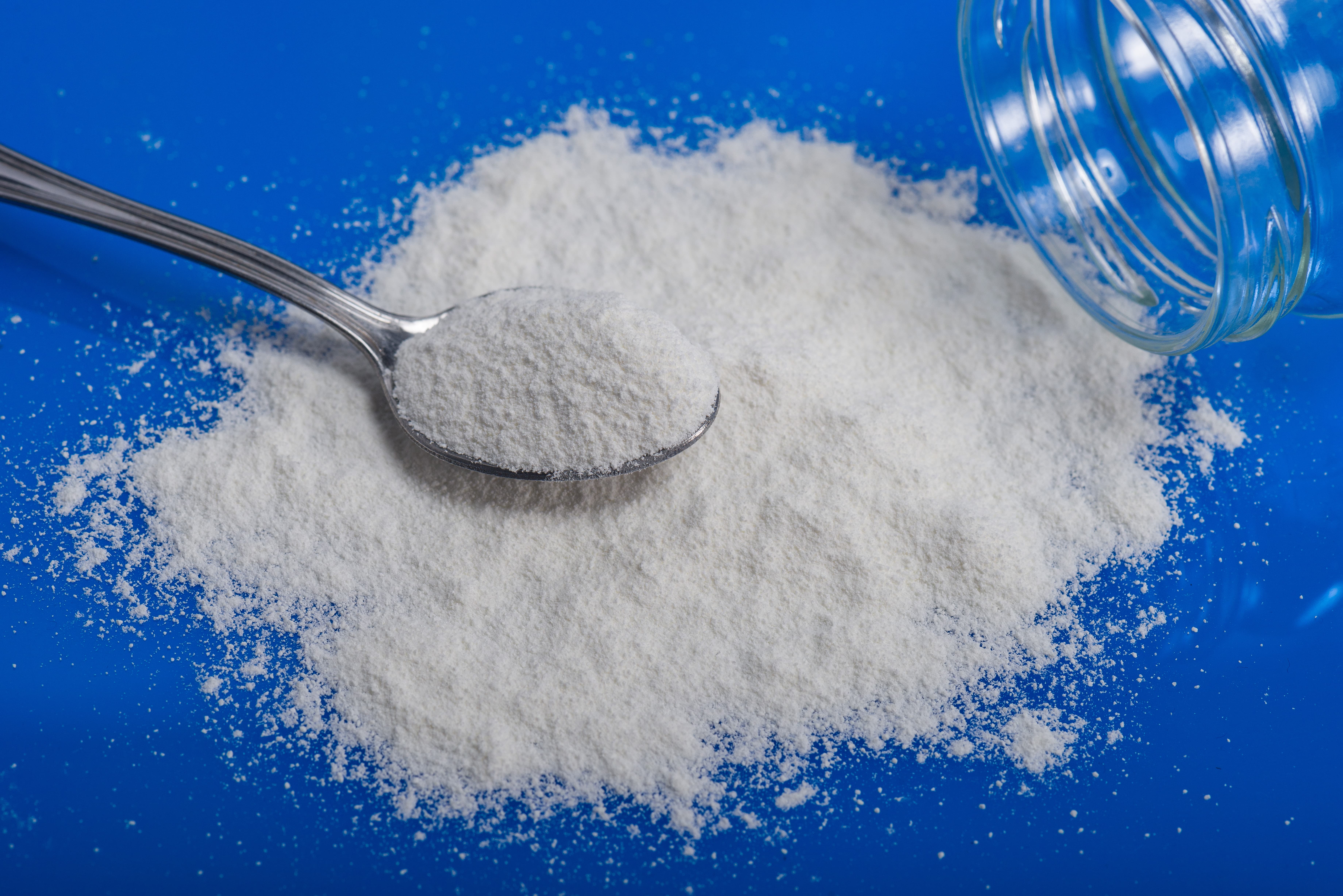 Ammonium Bicarbonate with a spoon on blue table.