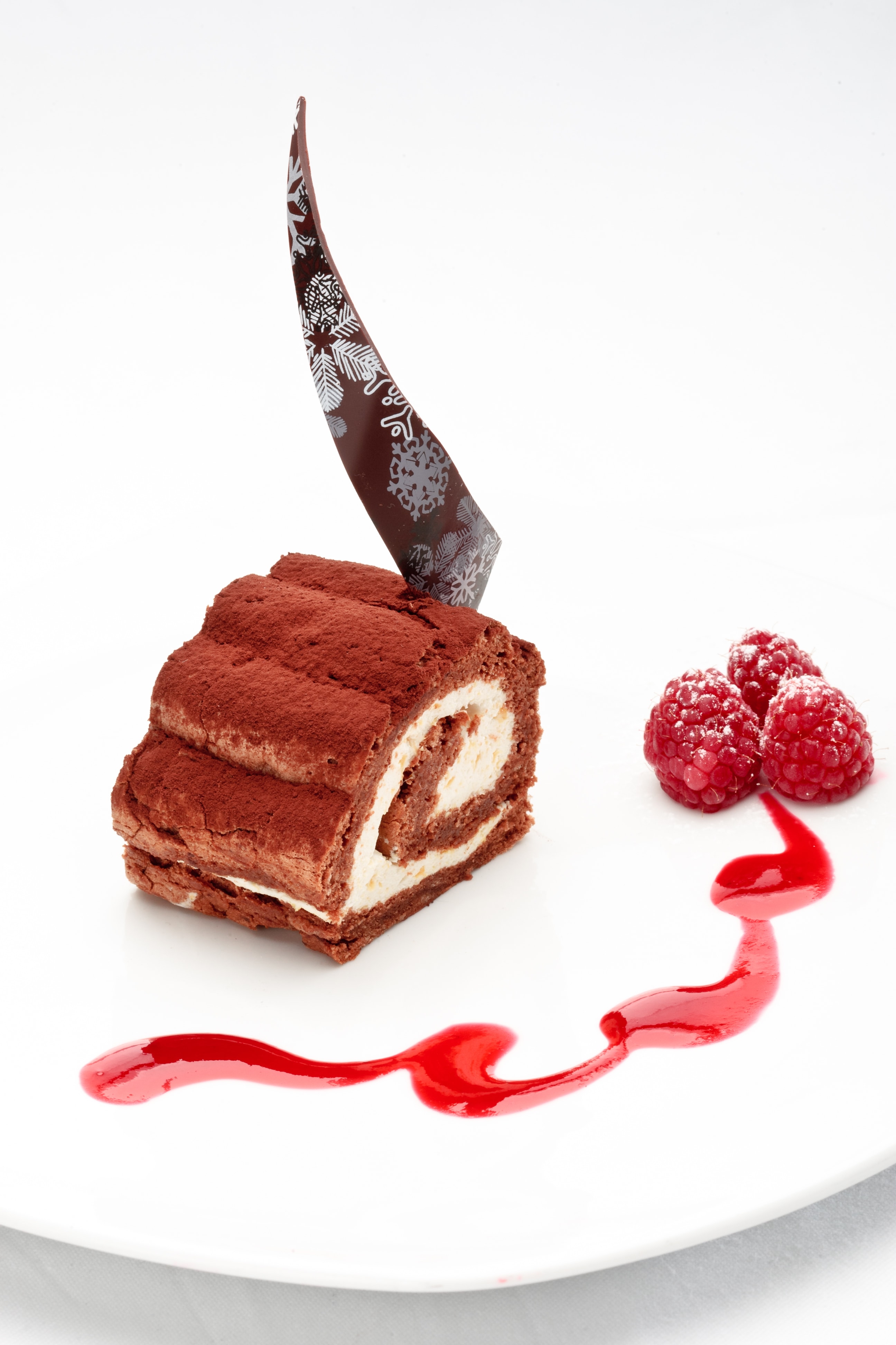 Chocolate roll with curd and mango cream decorated with raspberry and sauce on a white background.